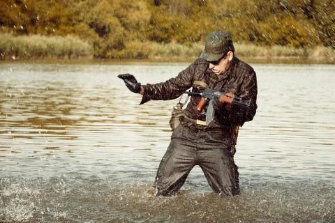 Soldier in uniform attacking in river with assault rifle Stock Photos