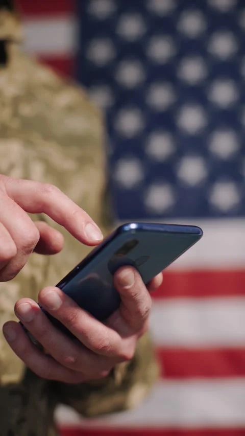 A soldier using a mobile phone in front of a U.S. flag. Stock Footage 327539993
