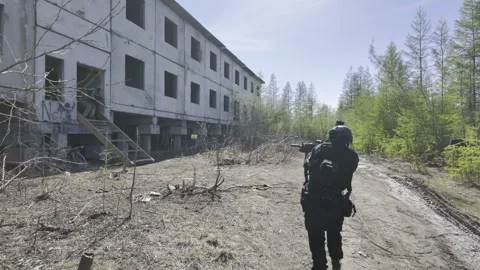 A soldier walks through a forest towards an abandoned building in the Vídeos de archivo 276834779