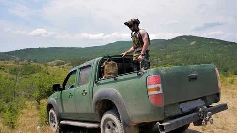 Soldier with weapon is sitting in the back of a pickup truck leaving the camp Stock Footage 129657475