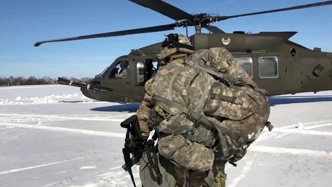 Soldier wearing full kit approaching Black Hawk helicopter waiting on snow Stock Footage 84972069