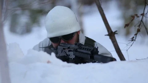 A soldier in a white hat is aiming for a weapon from behind a snowdrift Stock Footage 83175941