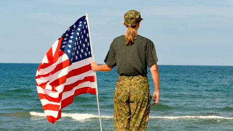 Soldier woman salute with American flag near sea . Slow motion, back view Stock Footage