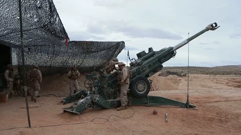 Soldiers load M777 howitzer from under camo net 3 Stockbeeldmateriaal 112128127