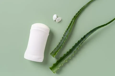 Solid antiperspirant deodorant and fresh aloe leaf over green background. Stock Photos