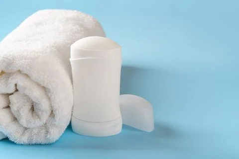 Solid antiperspirant deodorant and rolled bath towel on a blue background. 스톡 사진