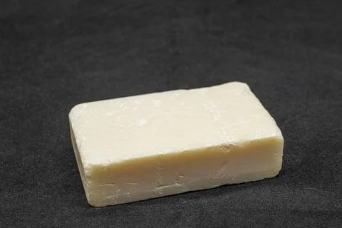 Solid bar of creamy, off-white soap rests on dark surface 库存照片