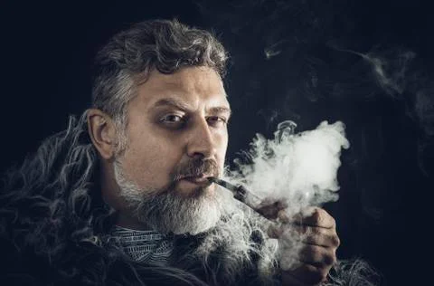 Solid bearded man in a fur mantle smoking pipe Stock Photos