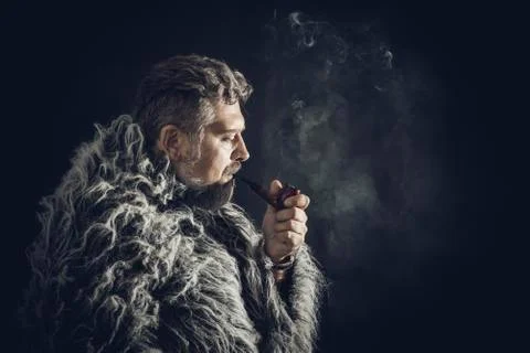Solid bearded man in a fur mantle smoking pipe Stock Photos