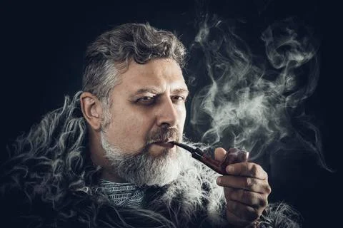 Solid bearded man in a fur mantle smoking pipe Stock Photos