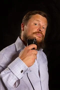 Solid beared man shaving by electric razor studio portrair on black background. Foto stock