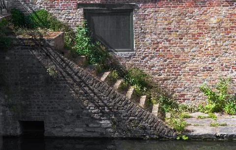A solid brick wall featuring a window and stairs leading up to it Stock Photos