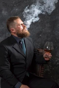 Solid confident bearded man in suit with glass of whisky and fume Stock Photos