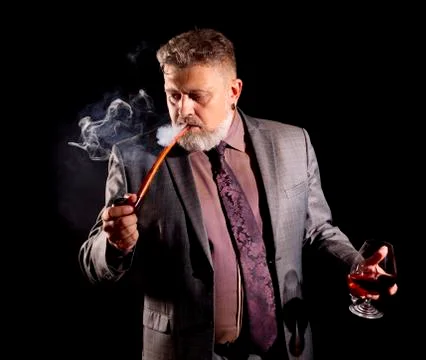 Solid confident bearded man in suit with glass of whisky smoking pipe Stock Photos