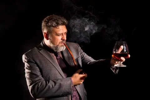 Solid confident bearded man in suit with glass of whisky smoking pipe Stock Photos