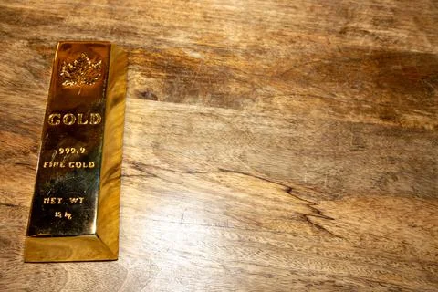 A solid gold bar on a wooden table Stock Photos