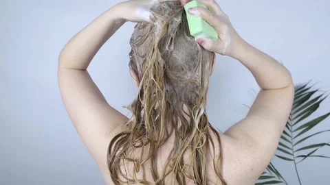 Solid hair shampoo. Close-up of a blonde girl in the bathroom, which lathers her Stock Footage 180557615