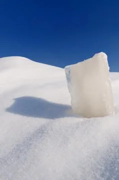 Solid ice cube, snowdrift and cloudless blue sky Stock Photos
