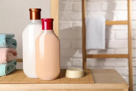 Solid shampoo bar and bottles of cosmetic product on wooden table in bathro.. 스톡 사진