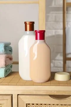 Solid shampoo bar and bottles of cosmetic product on wooden table in bathroom Stock Photos