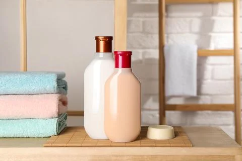 Solid shampoo bar and bottles of cosmetic product on wooden table in bathroom Stock Photos