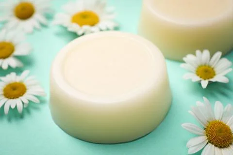 Solid shampoo bar and chamomiles on turquoise background, closeup Stock Photos
