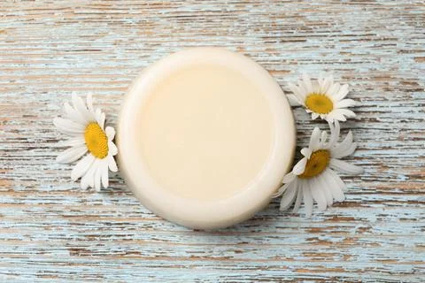 Solid shampoo bar and chamomiles on light wooden table, flat lay. Hair care Foto stock