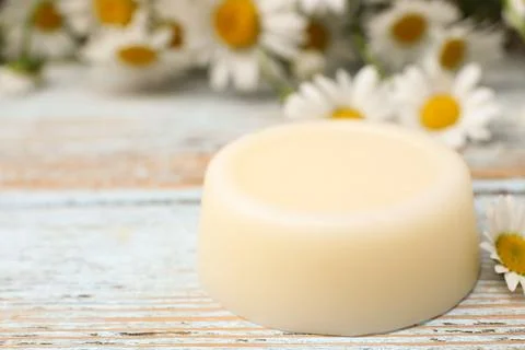 Solid shampoo bar and chamomiles on light wooden table, closeup. Space for te Foto stock