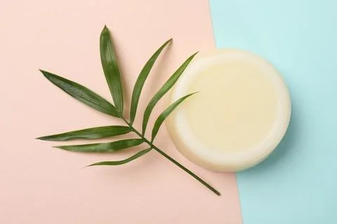Solid shampoo bar and green leaf on color background, top view. Hair care Foto stock