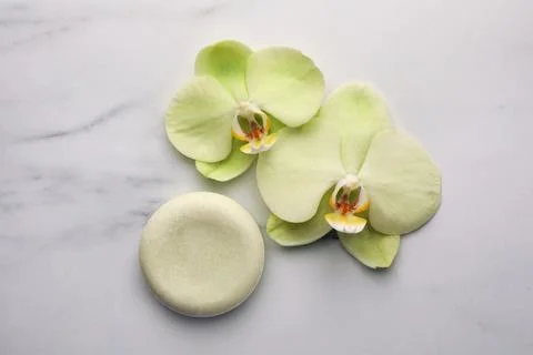 Solid shampoo bar and orchid flowers on white marble table, flat lay. Spa c.. 스톡 사진