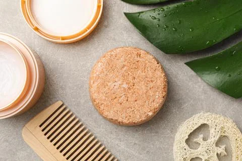Solid shampoo bar, cream, monstera leaf, comb and loofah on grey table, flat  Foto stock