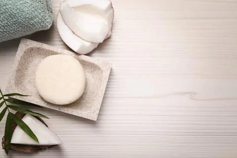 Solid shampoo bar, leaf and coconut on white wooden table, flat lay. Space fo Foto stock