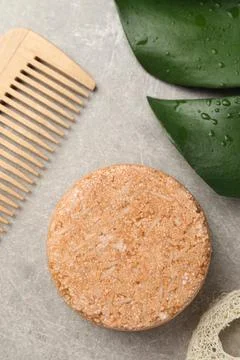 Solid shampoo bar, monstera leaf and comb on grey table, flat lay Stock Photos