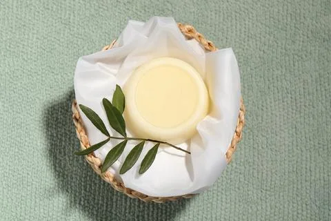 Solid shampoo bar in wicker basket on pale green fabric, top view 스톡 사진