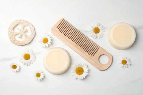 Solid shampoo bars, comb and chamomiles on white marble table, flat lay. Hair 写真素材