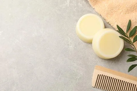 Solid shampoo bars, towel green twigs and comb on grey table, flat lay. Spa.. Stock Photos