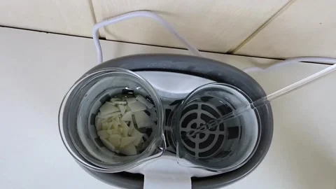 Solid soy wax flakes melting into a clear liquid inside a glass beaker in an Stock Footage 337738147