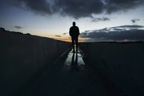Solitary man walking at sunset with dramatic sky Stock Photos