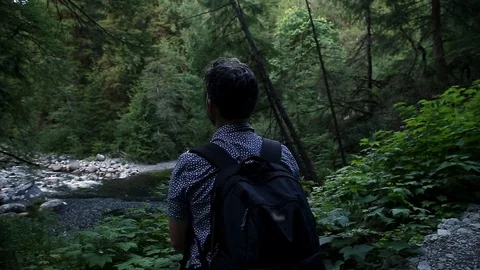 A solitary middle aged man with a backpack looking out at a river in an Stock Footage 115332945