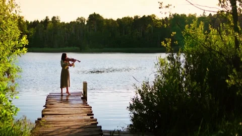 Solitary violinist performing at sunset on a rustic wooden dock beside a Stock Footage 340225146