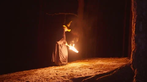 A solitary wizard walks through a dense forest at night, holding a torch that Video stock 306328255