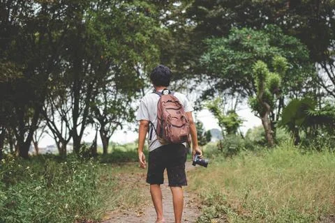 Solo backpacker with camera in hand walks alone. Back view photo of travele.. Stock Photos