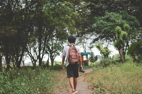 Solo backpacker with camera in hand walks alone. Back view photo of travele.. Stock Photos