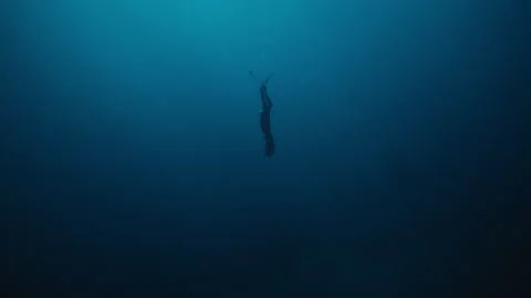 Solo free diver descends into deep ocean depths as dark silhouette in slow Stock Footage 325692571