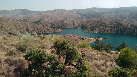 Solo hiker walking down arid mountain trail towards vast blue reservoir, em.. Stock Footage 341828737