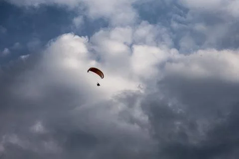 Solo paraglider soaring through dramatic clouds against a blue sky Stock Photos