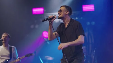 Soloist popular pop group performs on stage in black round glasses and black Stock Footage 244489948