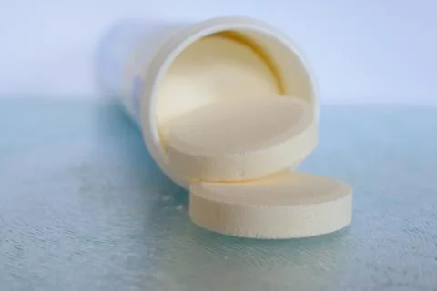 Soluble tablets falling out the plastic tube on glass table top - closeup. Sh Stock Photos