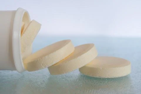 Soluble tablets falling out the plastic tube on glass table top - closeup. Sh Stock Photos