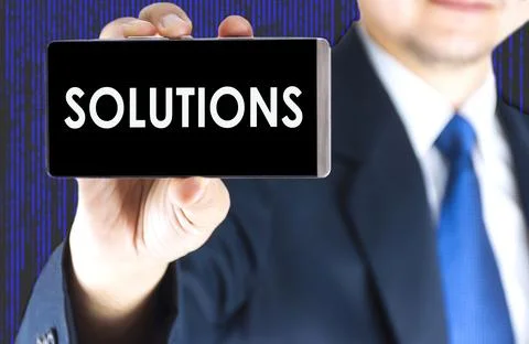SOLUTIONS word on mobile phone screen in blurred young businessman hand and.. Фото
